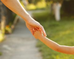 close up of parent holding hands with child and walking outside.
