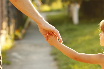 close up of parent holding hands with child and walking outside